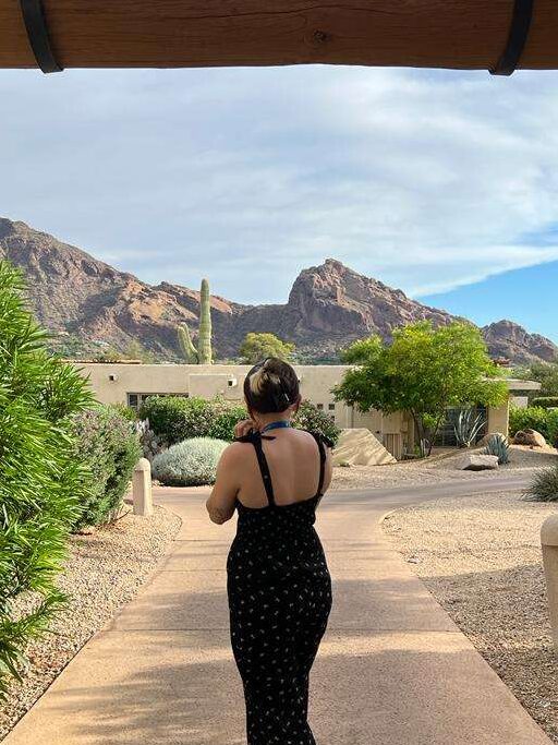Alyssa standing in a scenic Arizona resort, with a mountain range and a stunning desert home in the background.